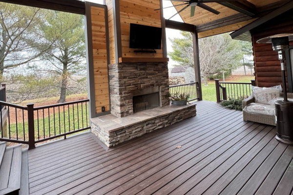 Covered outdoor deck with a stone fireplace, mounted TV, and ceiling fan