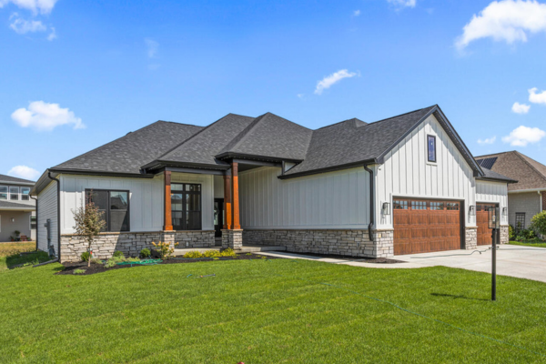New construction home with white board and batten siding, stone foundation, and wood garage door
